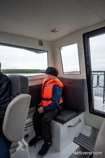 A child in an orange life jacket sits on a boat, looking out a large window. The scenery outside is blurred.